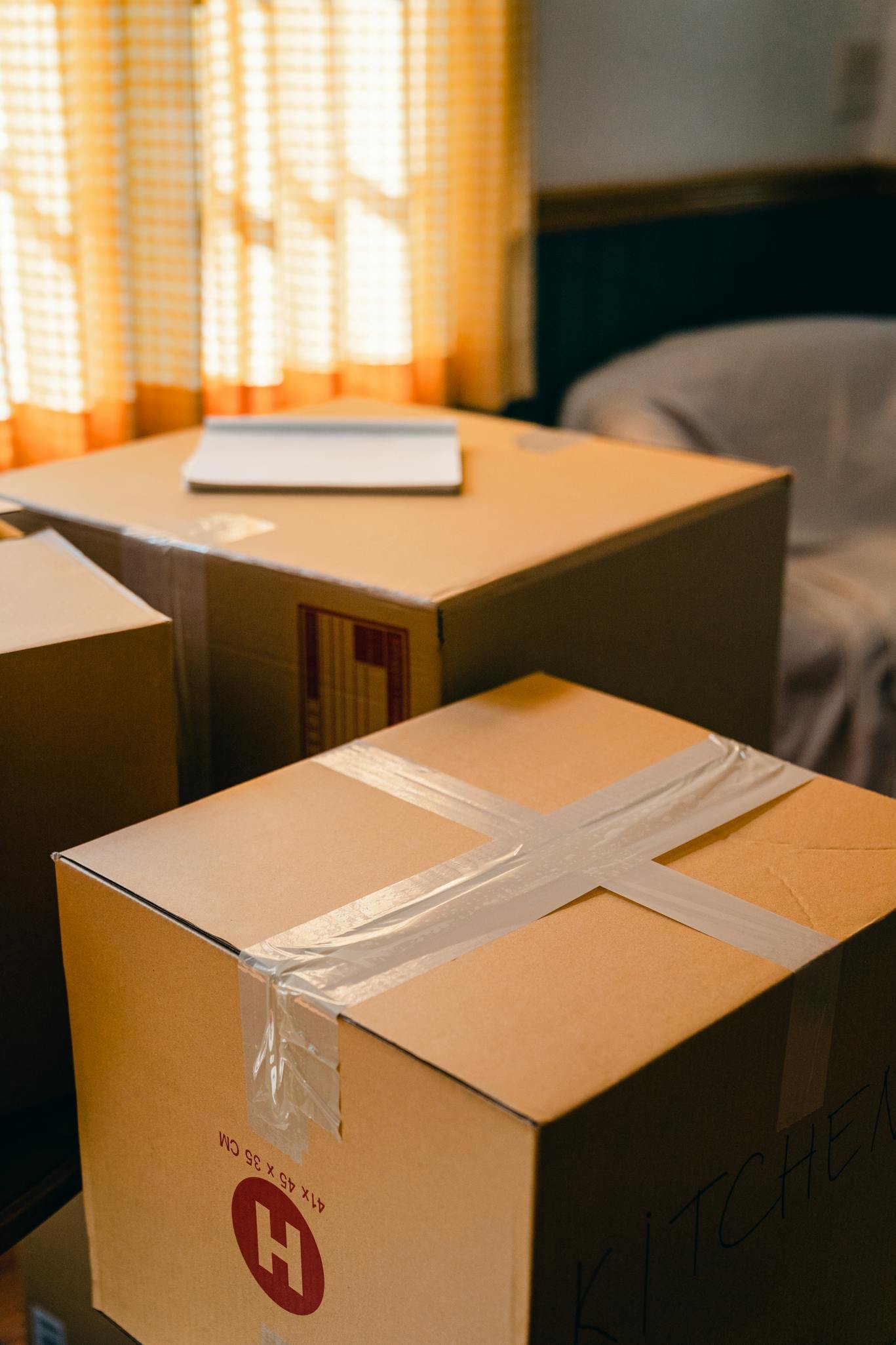 From above of cardboard boxes with notebook sealed with tape placed in room near blinded window on sunny day